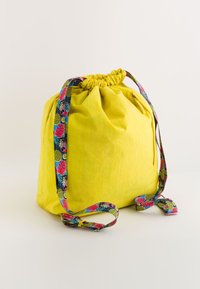 Geantă de umăr galbenă cu șnur, având o parte superioară strânsă, prezentând o curea cu un model în nuanțe de albastru, roz și verde. Textură moale și design casual.
