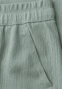 Hellgrüner strukturierter Stoff mit einem elastischen Bund und einer schrägen Seitentaschen-Nahtdetail.