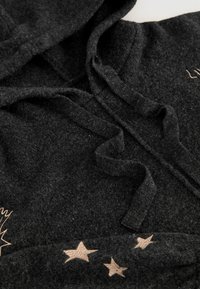 Schwarzer Fleece-Hoodie mit Kordelzug, weichem Material und bestickten Sternen in einem helleren Farbton am unteren Saum.