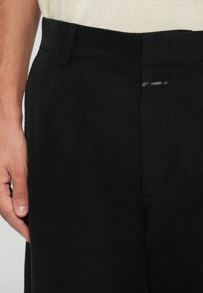 Pantalones negros con una textura suave, que cuentan con un bolsillo delantero y una pequeña etiqueta "CLOSED" en la cintura.