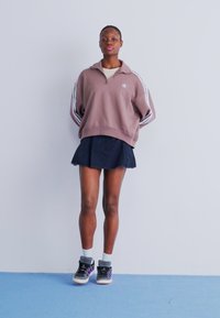 Sweatshirt oversized em cor malva com riscas brancas, saia mini preta e ténis pretos com detalhes em roxo. Design simples, ajuste descontraído.