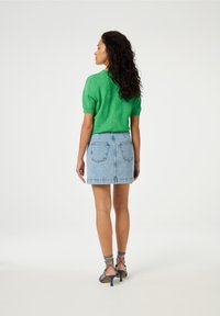 Groene gebreide trui met korte mouwen en textuurpatroon, gecombineerd met een lichtblauwe denim mini-jurk en blauwe hakken met bandjes.