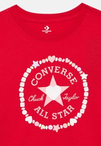 Κόκκινο βαμβακερό μπλουζάκι με κεντρικό λευκό αστέρι με καρδιά, περιτριγυρισμένο από κείμενο και πολύχρωμες κουκκίδες, με διακοσμητικά παιχνιδιάρικα σχέδια.