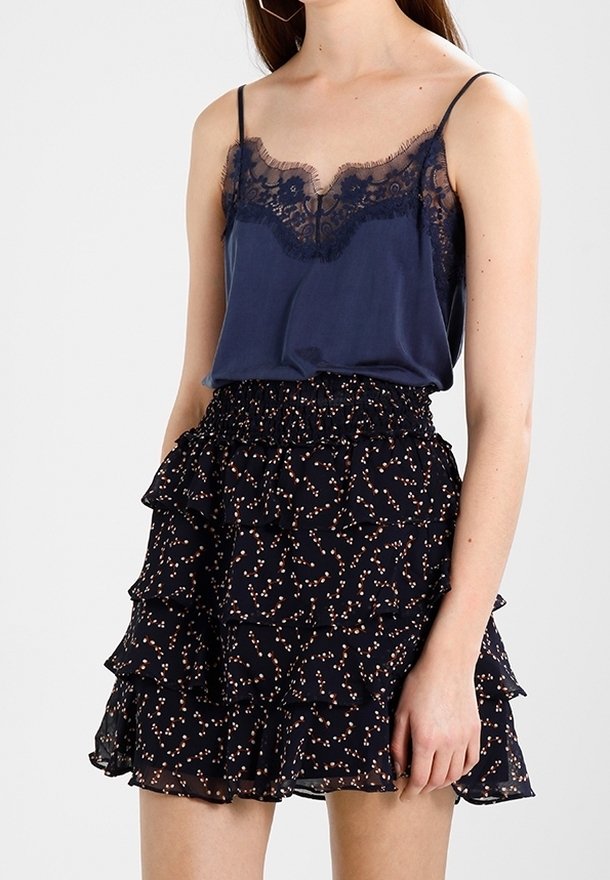 Femme portant un caraco bleu marine orné de dentelle et une mini-jupe noire à volants avec un petit motif floral.