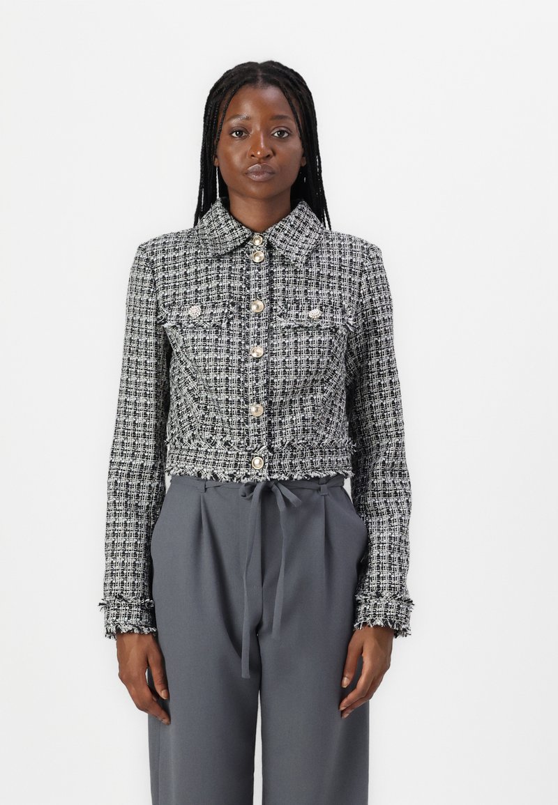Jakku tweed hitam-putih bermotif dengan kerah, penutup kancing, dan kantong depan. Dipadukan dengan celana abu-abu tinggi di pinggang.