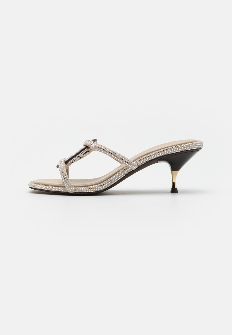 Heeled sandal with a nude fabric upper, embellished with clear rhinestones. Features a thin strap design and a black heel with a gold accent.