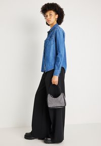 Camisa de ganga com dois bolsos no peito, corte oversize; calças largas pretas; pequena bolsa prateada brilhante com forma arredondada e alça preta.