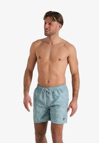 Zwemshorts in lichtblauw met een bladerenpatroon, voorzien van een elastische tailleband met trekkoord en een klein logoopdruk aan de onderkant aan de linkerzijde.