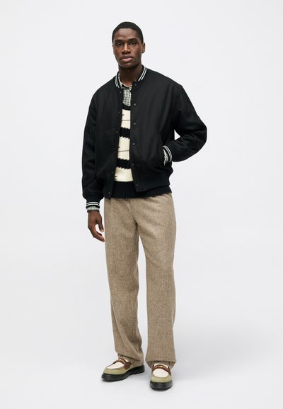 Crna bomber jakna s prugastim manžetama, nosi se preko bijele i crne prugaste serafine. Smešani, teksturirani hlače i šarene cipele.