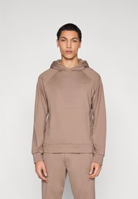 Φούτερ με κουκούλα Nike σε ανοιχτό καφέ χρώμα με τσέπη καγκουρό, κουκούλα με κορδόνια και υφασμάτινη υφή. Διαθέτει μικρό λογότυπο στο στήθος και ριμπ μανσέτες.