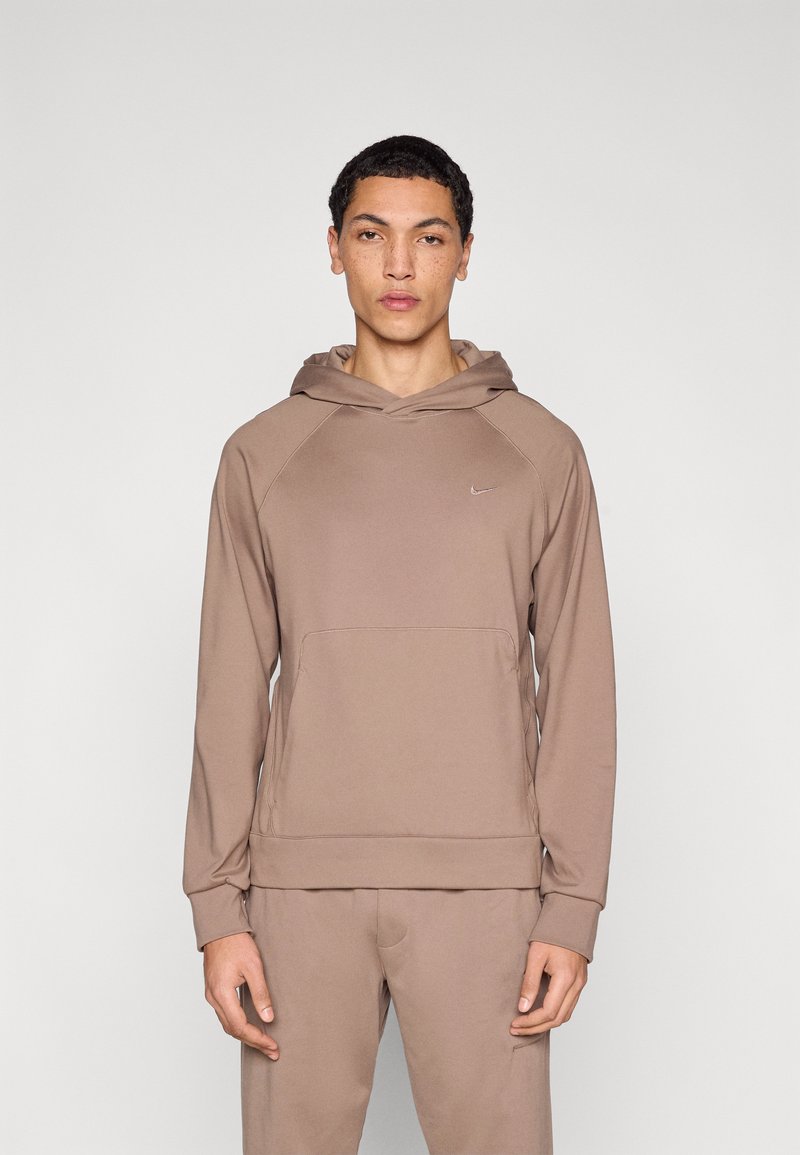 Φούτερ με κουκούλα Nike σε ανοιχτό καφέ χρώμα με τσέπη καγκουρό, κουκούλα με κορδόνια και υφασμάτινη υφή. Διαθέτει μικρό λογότυπο στο στήθος και ριμπ μανσέτες.