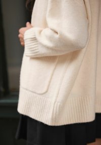 Beige vest van een wollen mix met een geribbelde zoom en manchetten, voorzien van een voorzak en een losse pasvorm. De textuur ziet er zacht en comfortabel uit.