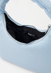 Ljusblå syntetisk handväska med rundad design, dragkedjestängning, silverfärgad maskinvara och en svart tygfoder med en varumärkesetikett.
