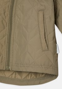 Kvadrafin grön jacka med dragkedja, diagonalmönster och sidficka. Slät tyg med glänsande yta och förstärkt nederkant.