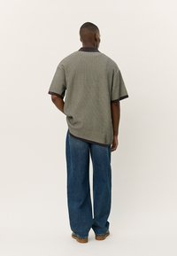 Kortermet strikket polo skjorte i grønn og svart striper, med mørk krage og kontrastkanting. Kombinert med vide blå denimbukser.