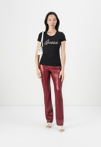Must have must, mille täpse musta särke, front zero "Guess" logo, koos punaste faux nahast laienevate pükstega. Mudel hoiab väikest valget kotti ja kannab kergeid sandaale.