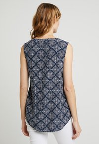 Top senza maniche blu navy con un design bianco a fantasia, scollo rotondo e orlo curvo, realizzato in tessuto leggero.