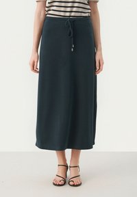 Jupe maxi vert foncé en tissu doux, dotée d'une taille élastique à cordon et d'une silhouette droite. Portée avec des sandales noires à lanières.