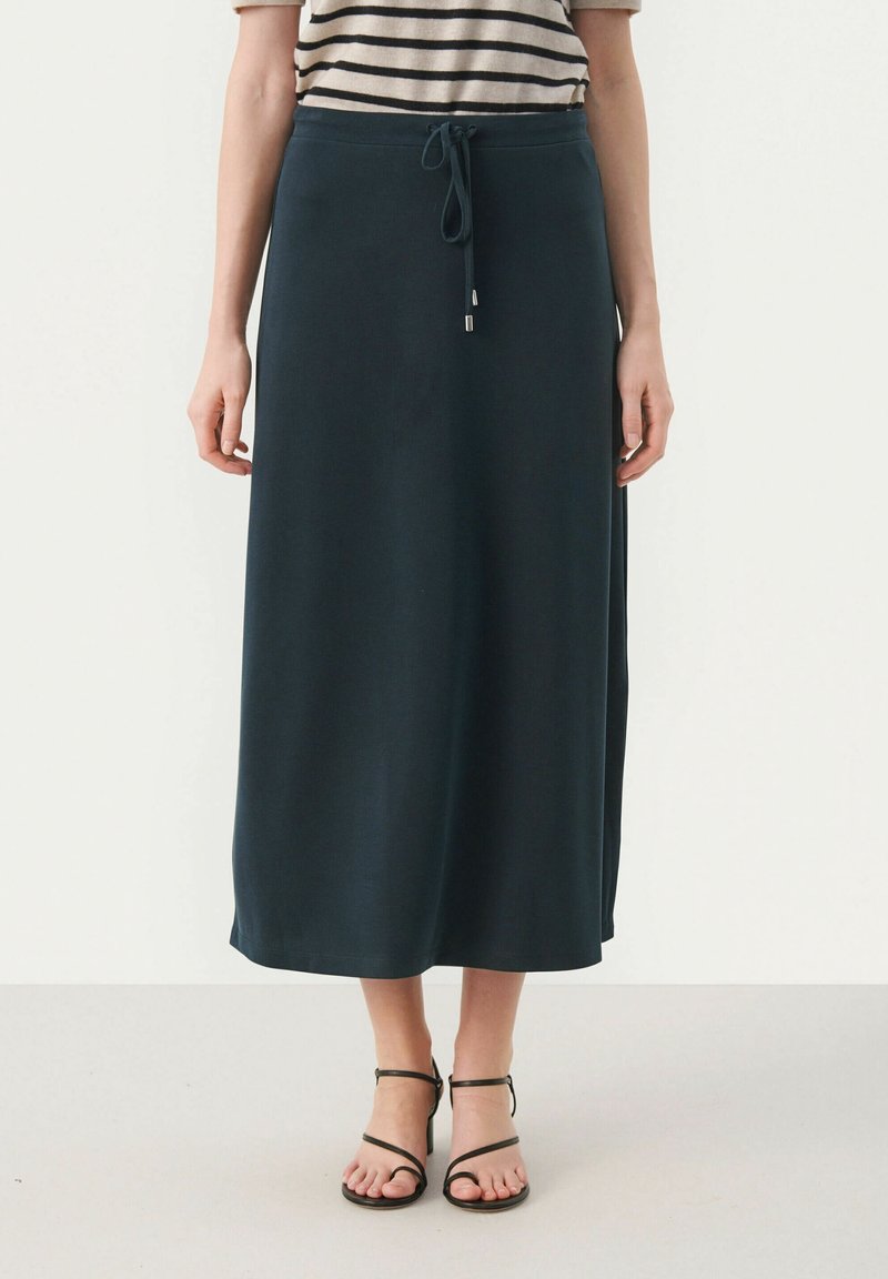 Jupe maxi vert foncé en tissu doux, dotée d'une taille élastique à cordon et d'une silhouette droite. Portée avec des sandales noires à lanières.