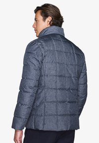 Giubbotto imbottito in tessuto blu scuro, con un design trapuntato, colletto alto e materiale testurizzato. La vista posteriore mostra una silhouette strutturata.