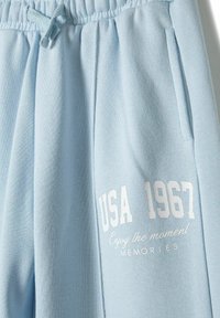 Ljusblå sweatshirtbyxor med elastiskt midjeband och dragsko. Har vit text: "USA 1967 Njut av stunden" samt två sidofickor.