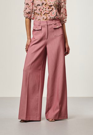 Wijde roze broek met hoge taille en verbonden klepzakken, gedragen met een top van bloemenkant en sandalen.