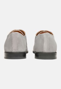 Chaussures en suède gris avec un bout arrondi et un petit talon en caoutchouc noir. Présentent deux détails de couture à l'arrière et une texture lisse sur le dessus.