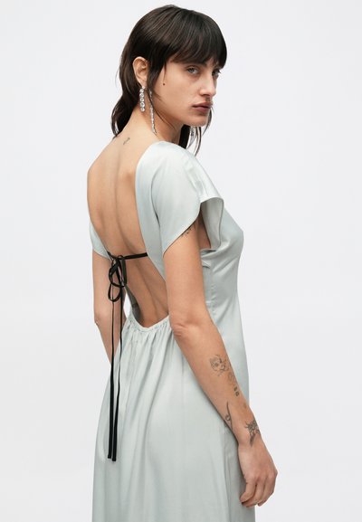 Svetlozelené saténové šaty s krátkymi rukávmi, otvoreným dizajnom na chrbte zabezpečeným čiernymi stuhami, s nazbieraným pásom.