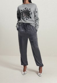 Pull gris avec un grand flocon de neige noir en sequins et des accents d'étoiles. Associé à un pantalon gris foncé brillant et des chaussures à talons hauts argentées.
