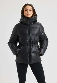 Zwarte pufferjack met hoge kraag en ritssluiting aan de voorkant, met een taillerende taille, een gladde textuur en een merklogo op de borst.