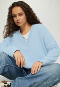 Lichtblauw sweater met een V-halslijn, geribbelde manchetten en een losse pasvorm, gecombineerd met high-waisted denim jeans. Gladde textuur en casual ontwerp.