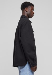 Zwarte wolmix overshirt met een kraag, knoopsluitingen bij de mouwen, zijslitsen en een enkel borstzakje, met een ontspannen pasvorm en een soepele textuur.