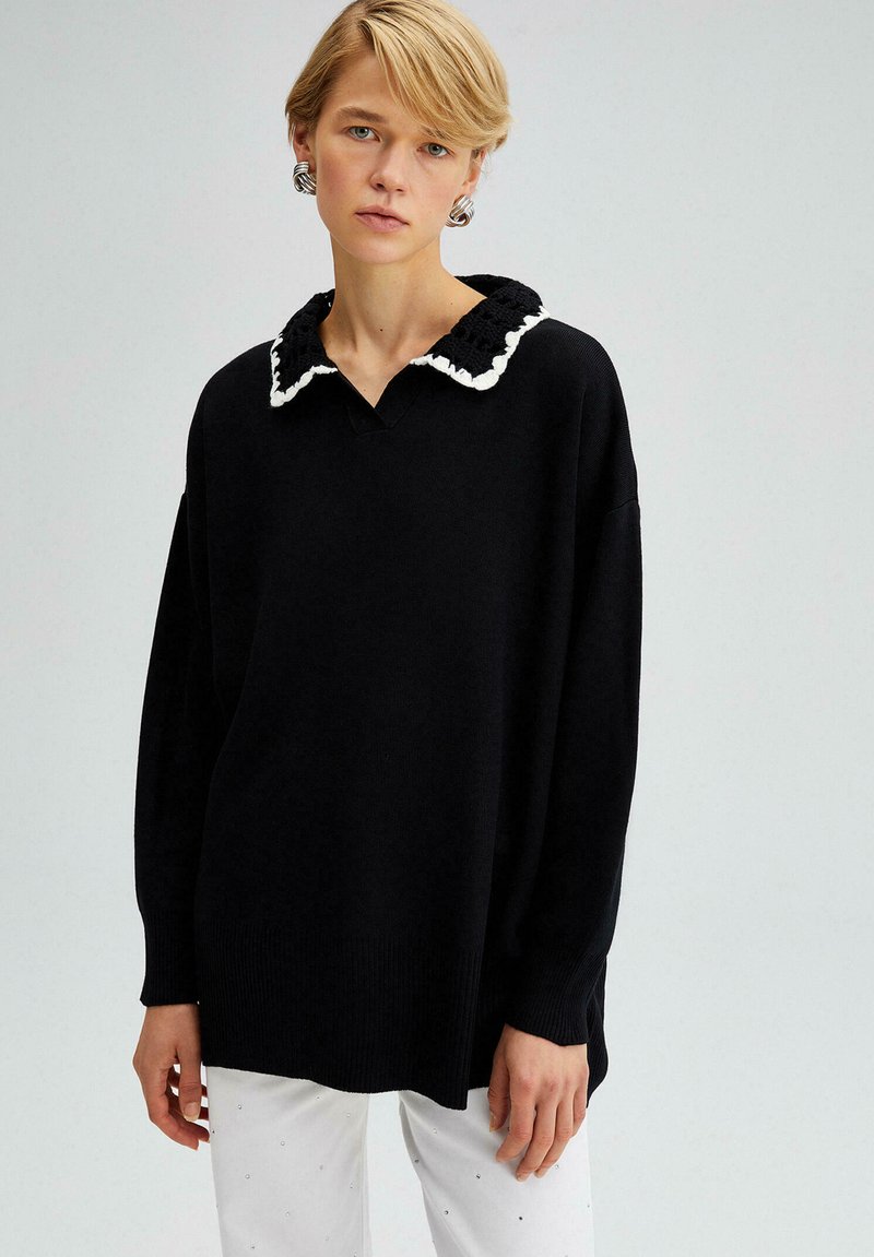 Maglione nero con un collare a volant testurizzato bianco, presenta una vestibilità ampia e maniche lunghe. Il tessuto è a coste e morbido.