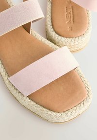 Roosa suede sandaalid kahe laia rihmaga, millel on vöödeldud jute platvorm ja sile pruun tallatoed mugavuse ja toetuse tagamiseks.