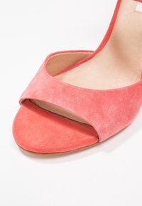 Sandale en daim rose corail à ouverture avant avec large bride frontale et semelle intérieure en cuir beige sur fond blanc.