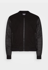 Zwarte bomberjack met een gestructureerd wollen lichaam en geplooide, glanzende nylon mouwen. Voorzien van een ritssluiting aan de voorkant en zijzakken met rits.