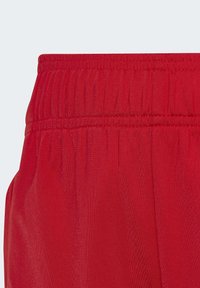 Rdeče kratke hlače iz tkanine z teksturiranim pasom, ki ima vodoravne črte in gladko površino. Material se zdi lahek in zračen.