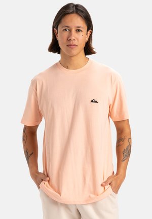 Camiseta de algodón de color rosa claro con cuello redondo, mangas cortas y un pequeño logo negro en el pecho izquierdo. Textura suave.