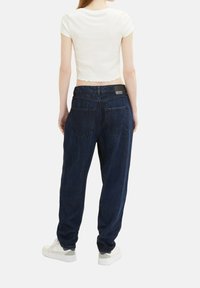 Jasnoszary krótki top i ciemnoniebieskie dżinsy o luźnym fasonie, pięciokieszeniowe, z białymi trampkami z szarymi akcentami.