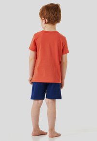 Rotes Baumwoll-T-Shirt mit kurzen Ärmeln und blauen Shorts. Der Stoff sieht weich aus und das Outfit ist für die Freizeit geeignet.