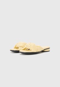 Gula platta sandaler med vävda remmar, med en texturerad yta och svart sula. Minimalistisk stil med öppen tå.