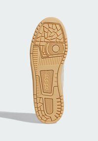 Potplat tenisice s teksturiranom gumenom površinom u bež boji, uz uzorak profila i vidljiv detalj brenda.