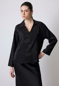 Top nero a maniche lunghe con scollatura a V e texture floreale, realizzato in tessuto morbido. Abbinato a una gonna in satin nera elegante.