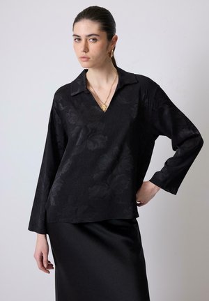 Black long-sleeve top with a V-neck and floral texture, made of smooth fabric. Paired with a sleek black satin skirt.