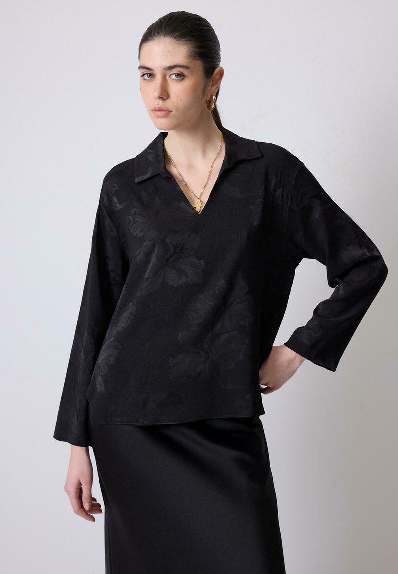 Top nero a maniche lunghe con scollatura a V e texture floreale, realizzato in tessuto morbido. Abbinato a una gonna in satin nera elegante.