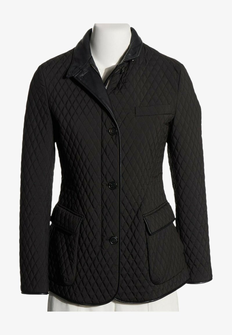 Veste matelassée noire avec fermeture par boutons, poches à rabat et col, présentée sur un torse de mannequin blanc.