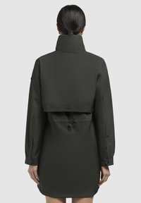 Jachetă impermeabilă de culoare verde închis, cu guler înalt, design în straturi pe spate, mâneci lungi și un cordon ajustabil la talie și în partea din spate.