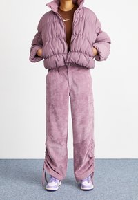 Vadderad lila jacka med hög krage, kombinerad med matchande vida, texturerade byxor och lila sneakers.