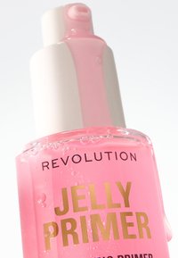 Botella de vidrio transparente con un primer de gelatina rosa, tapa de bomba blanca y texto dorado "REVOLUTION" y "JELLY PRIMER". Burbujas visibles en el producto.