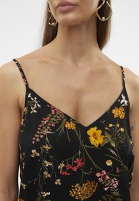 Camisola nera floreale con scollatura a V, caratterizzata da vivaci motivi di fiori gialli, rosa e verdi. Spalline sottili e regolabili, texture morbida.